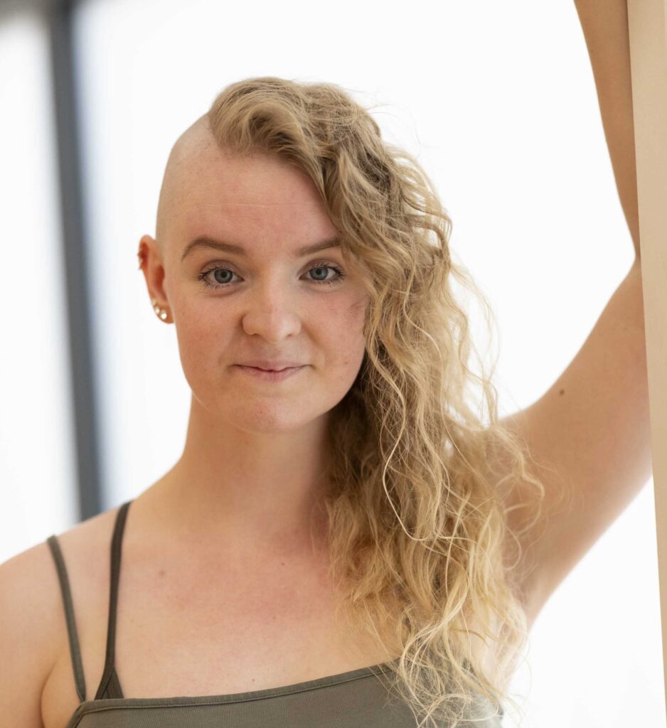Amanda lutar sig lätt mot en vägg och ler självsäkert in i kameran.